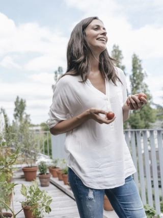 Frau steht auf ihrer Terrasse, schaut in die Ferne und hat kleine Tomaten in der Hand